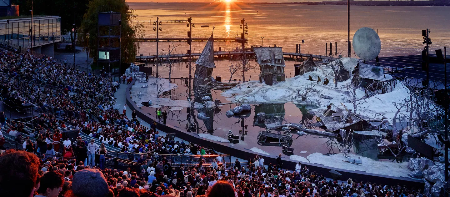 Seebühne der Bregenzer Festspiele bei Sonnenuntergang mit Publikum und einer Bühne, die wie eine zerfallene, weiße Landschaft gestaltet ist