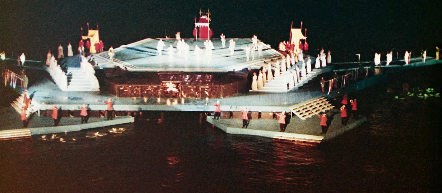 Szene aus "Die schöne Helena", 1966 auf der Seebühne, eine eckig gestaltete Plattform mit unterschiedlichen Höhenniveaus, die über Treppen miteinander verbunden sind, die Darstellenden sind auf verschiedenen Ebenen verteilt, teils in hellen, teils in roten Kostümen