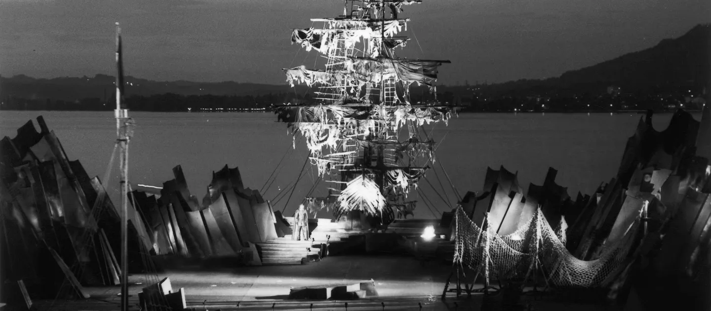 Szene aus "Der fliegende Holländer", 1973 auf der Seebühne, zentrale, leere Bühnenfläche ist von spitzen Felsen umgeben, im Hintergrund schließt mittig ein beleuchtetes Schiff an
