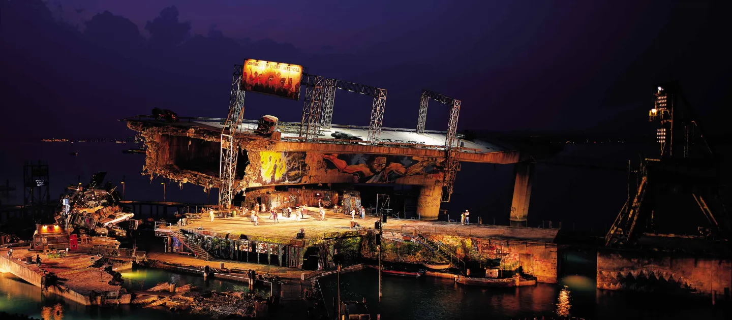 Szene aus "Porgy and Bess", 1998 auf der Seebühne, zerstörtes Brückenteil, bemalte Wände, ein Haufen aus Autos und ein paar kostümierte Darstellende 