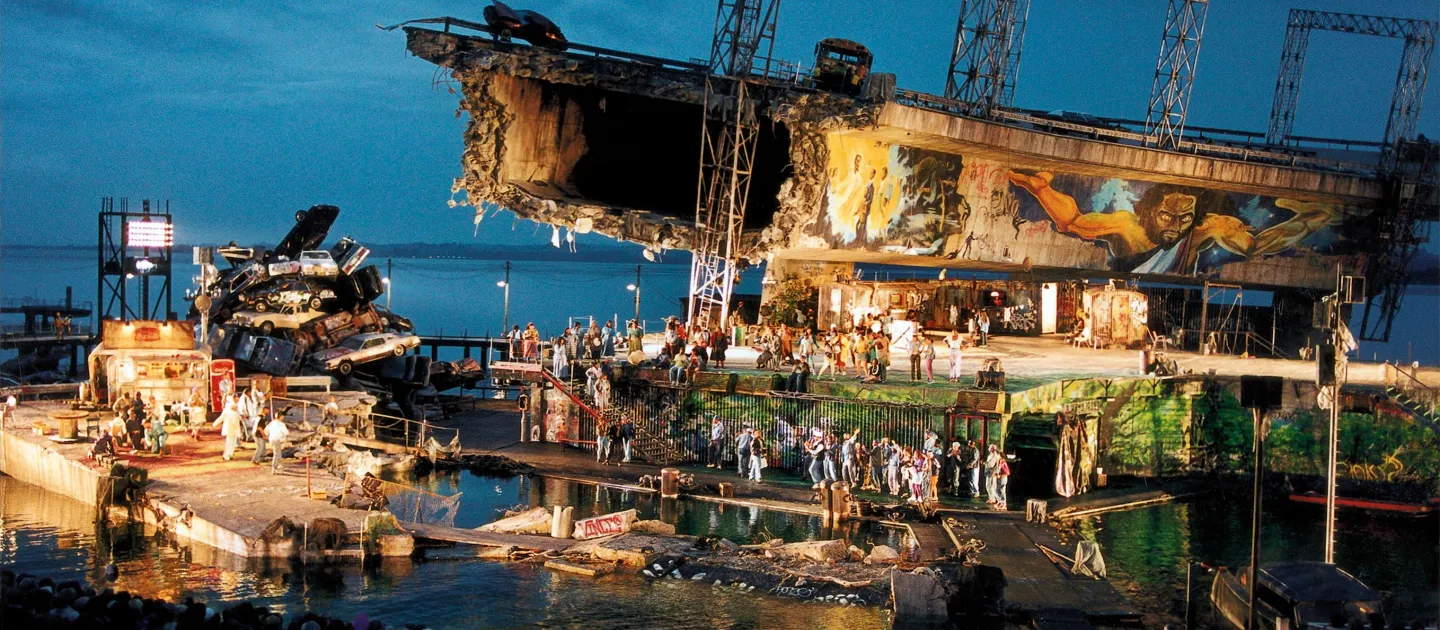 Szene aus "Porgy and Bess", 1997 auf der Seebühne, zerstörtes Brückenteil, bemalte Wände, ein Haufen aus Autos und viele kostümierte Darstellende 