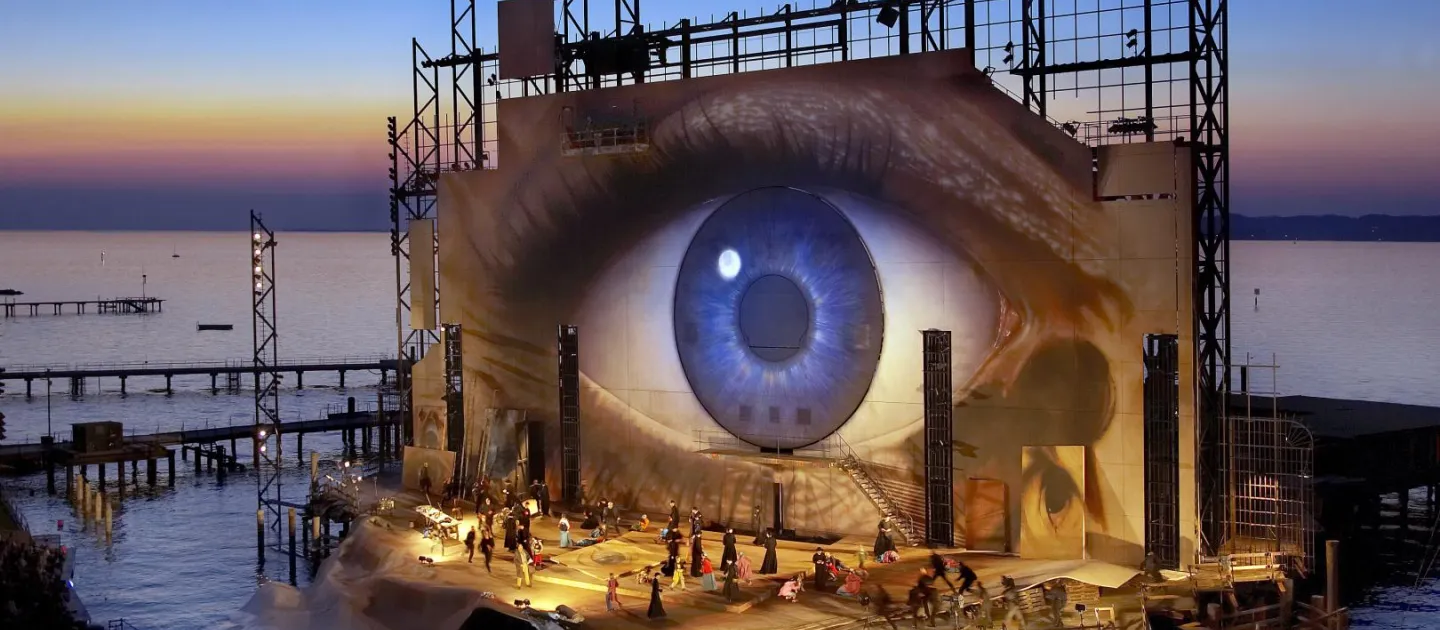 Szene aus "Tosca", 2007 auf der Seebühne, großes, flächendeckendes Auge auf der Rückwand, kostümierte Darstellende auf der Bühne