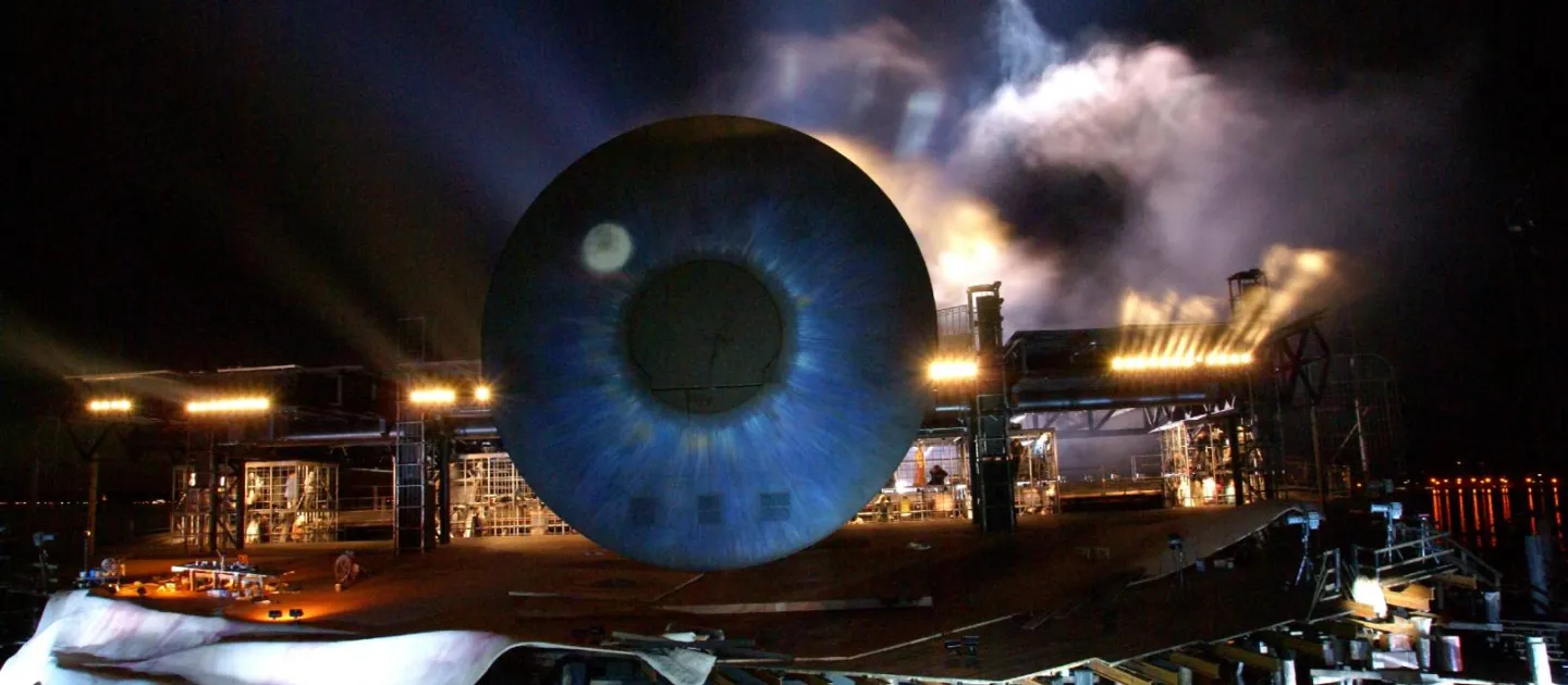 Szene aus "Tosca", 2008 auf der Seebühne, großes, blaufarbiges Auge, dahinter eine Gerüstkonstruktion und Nebel