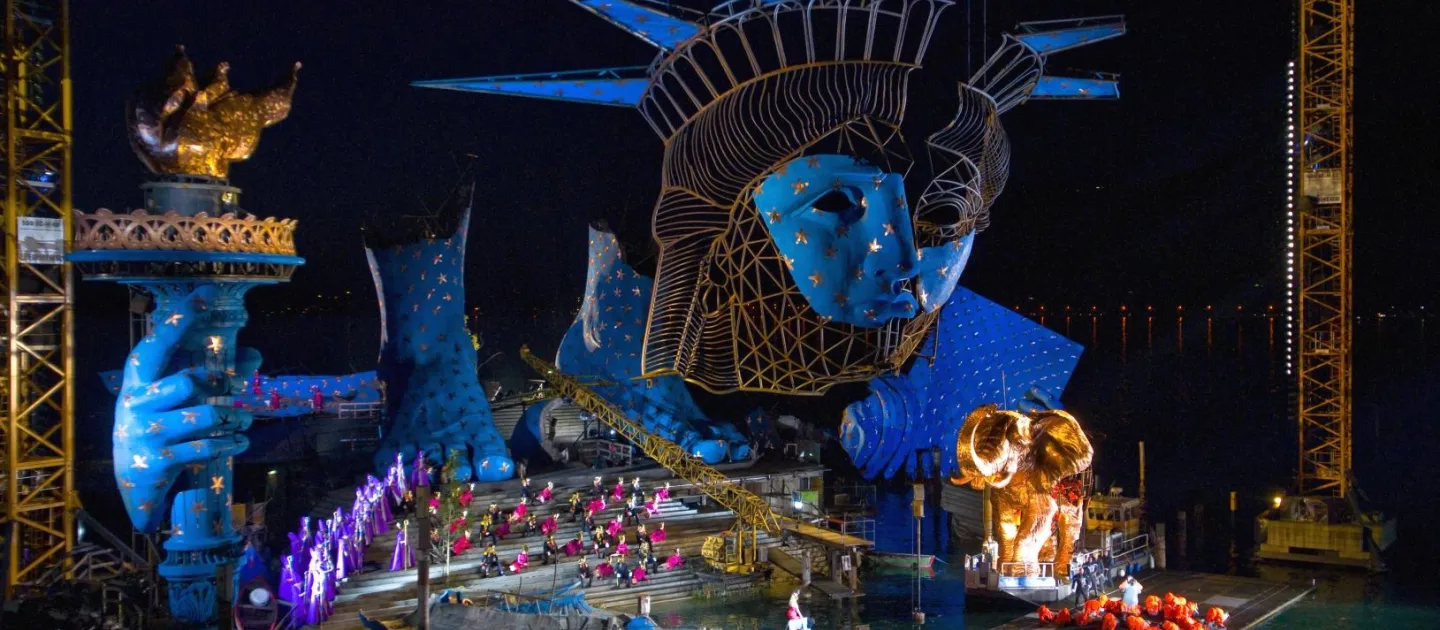 Szene aus "Aida", 2010 auf der Seebühne, Hintergrund mit großem blau-goldenen Freiheitstatue-Kopf und -Hand, viele kostümierte Darstellende und einem goldenen Elefanten