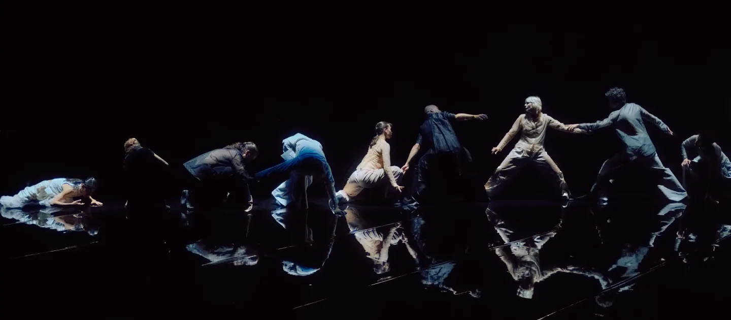 Tero Saarinen in einer modernen Tanzperformance, die sich in einer Linie mit dynamischen Posen auf einer reflektierenden schwarzen Bühne bewegen