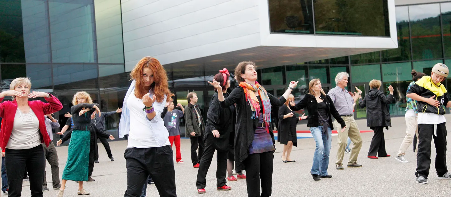 Szene aus "Der Beschwerdechor", 2011 auf dem Vorplatz des Festspielhauses, Gruppe von Menschen in Bewegung, im Hintergrund das Festspielhaus