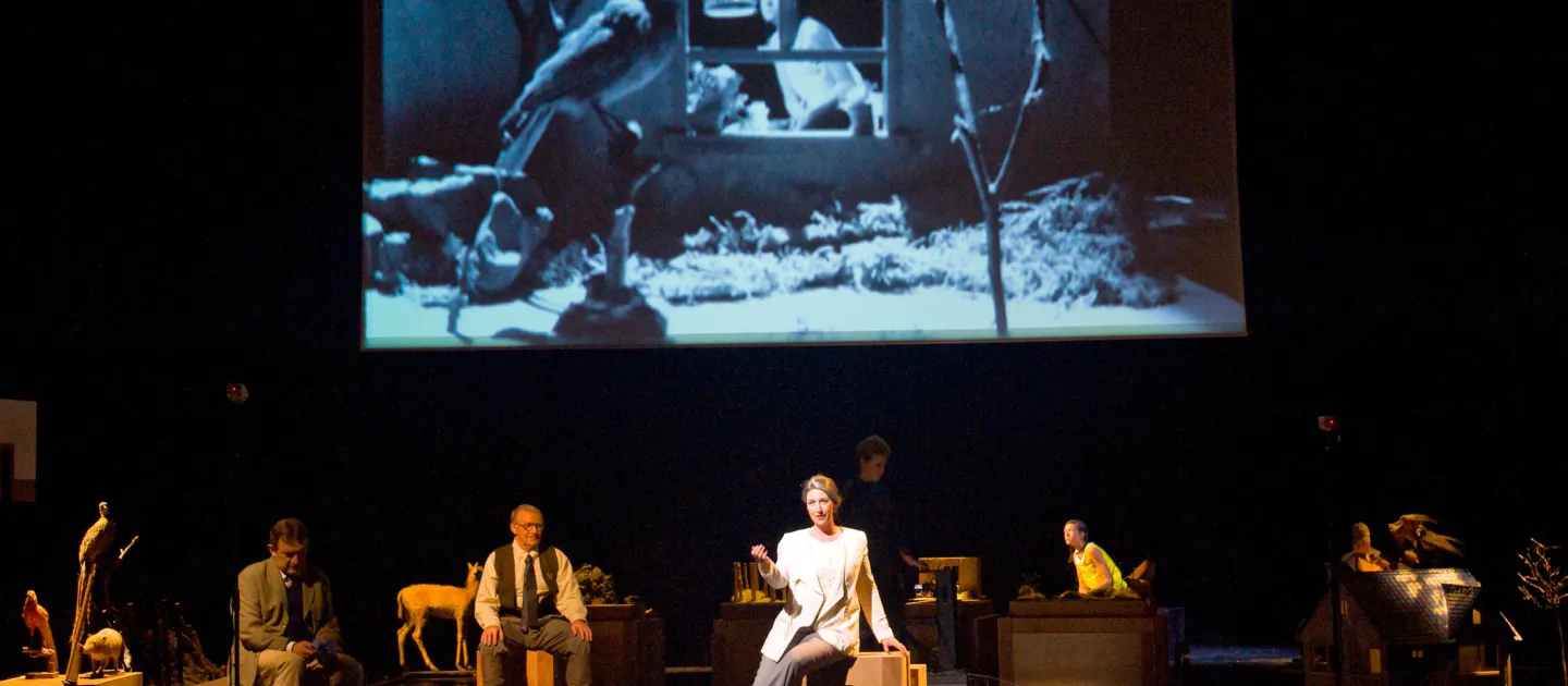 Szene aus "Der blonde Eckbert", 2011 im Theater am Kornmarkt, vier kostümierte Darstellende, drei im Vordergrund, einer im Hintergrund, im Hintergrund eine Leinwand mit einem schwarz-weißem Vogelbild