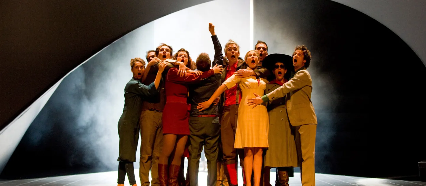Szene aus "Das Allerheiligste trifft das Allermenschlichste - Petite messe solennelle", 2012 im Festspielhaus, zehn kostümierte Darstellende auf der Bühne gruppiert, im Hintergrund Nebel, dunkle Wände und Lichtstimmung