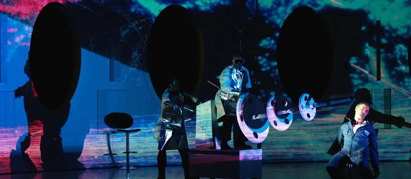 Szene aus "Solaris", 2012 im Festspielhaus, drei kostümierte Darstellende, bunte abstrakte Projektionen im Hintergrund