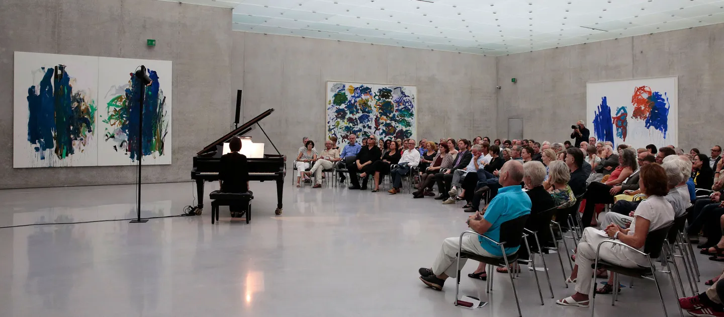 Szene aus "Konzert im KUB", 2015 im Kunsthaus Bregenz, Publikum sitzt auf Stühlen und blickt auf den Pianisten am Flügel, an den Wänden befinden sich großflächige Gemälde