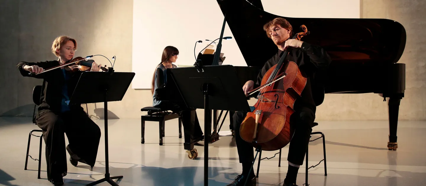 Szene aus "Konzert im KUB", 2016 im Kunsthaus Bregenz, drei Musiker:innen spielen die Instrumente Violine, Klavier und Cello 