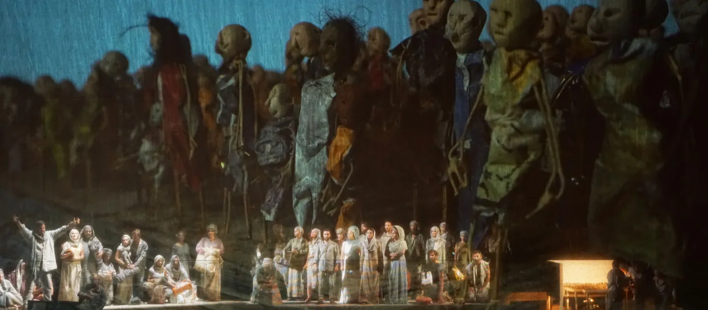 Szene aus "Moses in Ägypten", 2017 im Festspielhaus, im Vordergrund kostümierte Darstellende auf der Bühnenfläche, im Hintergrund übergroße Puppen