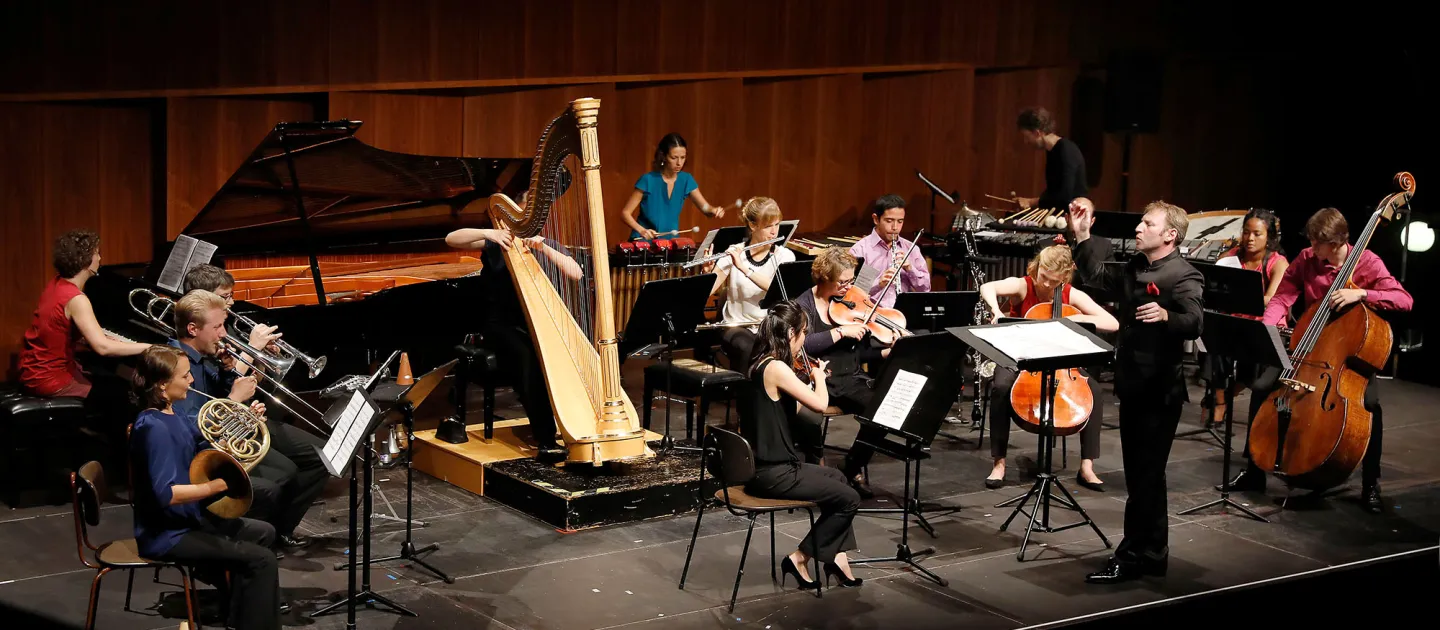 Szene aus "Opus XXI", 2017 im Festspielhaus, Musiker:innen auf der Bühne, Dirigent steht davor