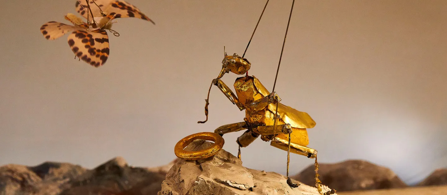 Szene aus "Ring in 90 Minuten", 2017 im Festspielhaus, goldfarbener Käfer als Marionette hält einen goldenen Ring, vor ihm schwebt ein Schmetterling mit braunen Flecken