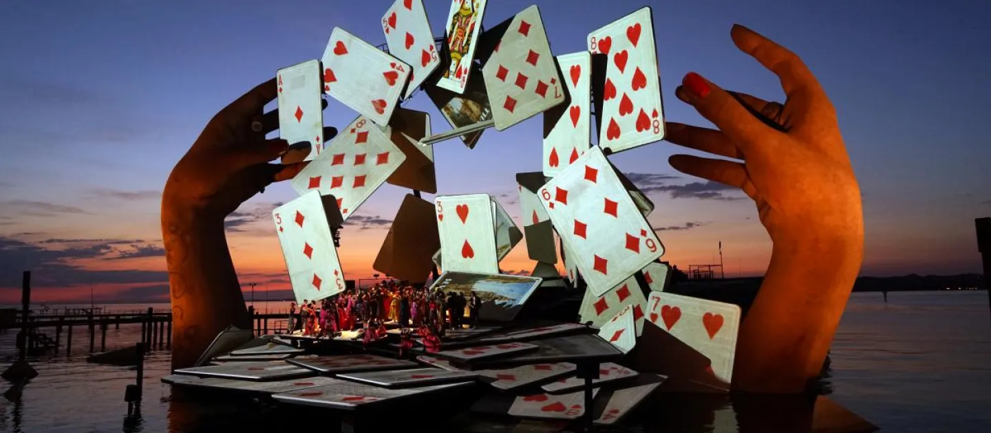 Szene aus "Carmen", 2017 auf der Seebühne, große Hände über dem Wasser, die Spielkarten in einem Bogen schweben lassen