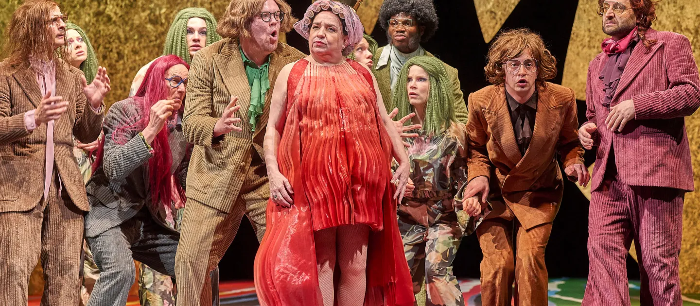Szene aus "Die gefesselte Phantasie", 2023 im Festspielhaus, elf kostümierte Darstellende, zentral eine Person in rotem Kleid und mit Krone auf dem Kopf