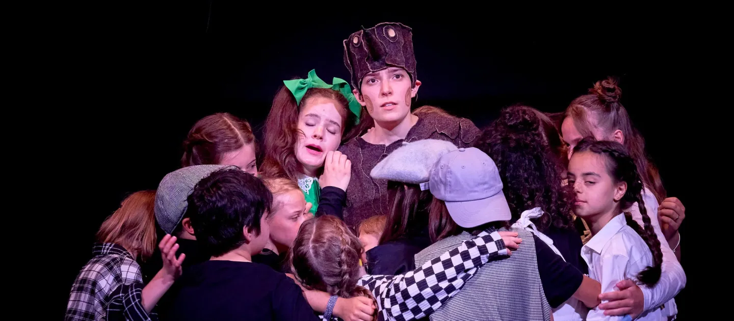 Szene aus "Pinocchio", 2024 im Theater Kosmos, Kinder in bunter Kleidung im Kreis stehend und sich umarmend