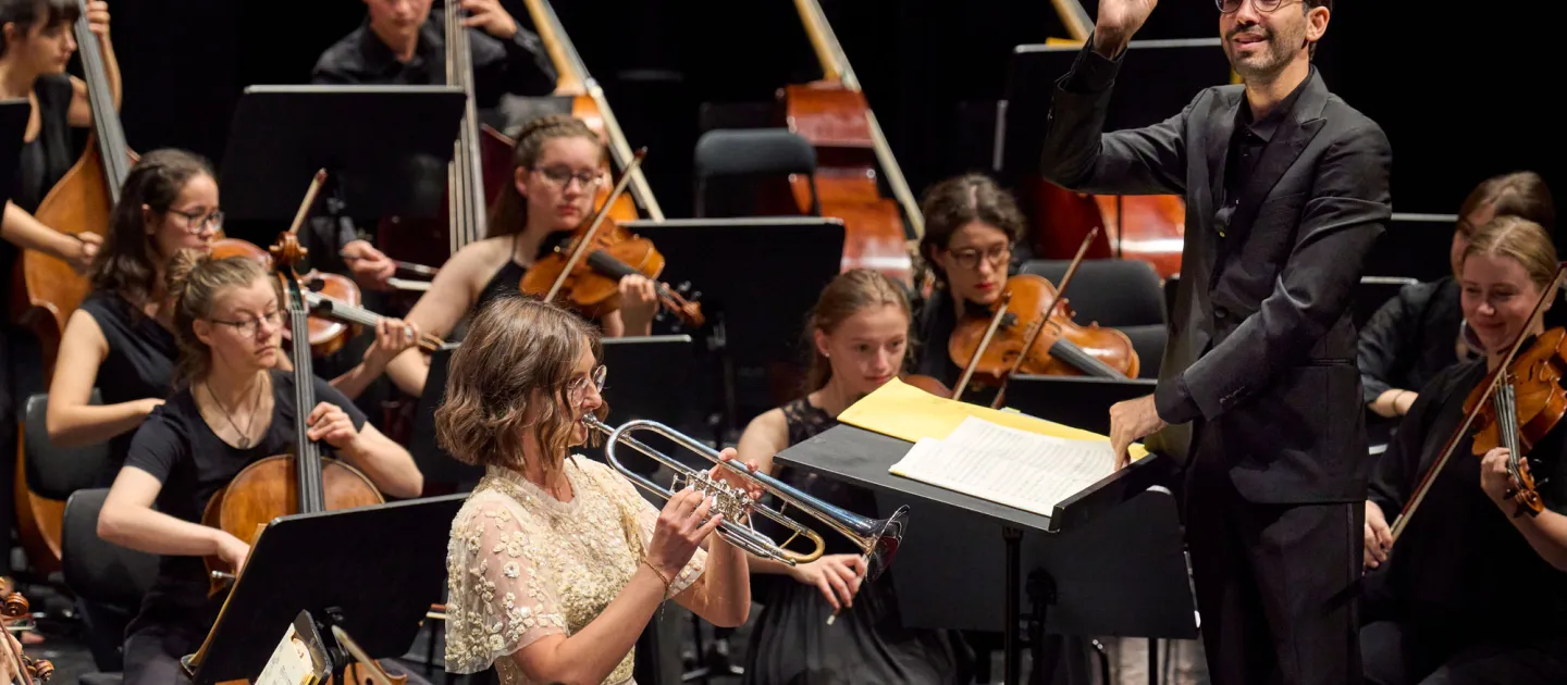 Szene aus "Orchesterakademie", 2022 im Festspielhaus, Ausschnitt des spielenden Orchesters, Dirigent hebt die rechte Hand