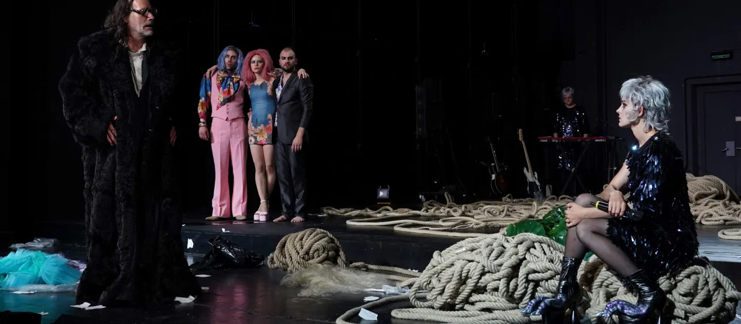 Szene aus "Der Sturm", 2022 im Theater am Kornmarkt, sechs kostümierte Darstellende, ein Mann mit schwarzem Pelzmantel, eine sitzende Frau mit grauem Haar und schwarzem Paillettenkleid, auf der Bühne liegen Seile