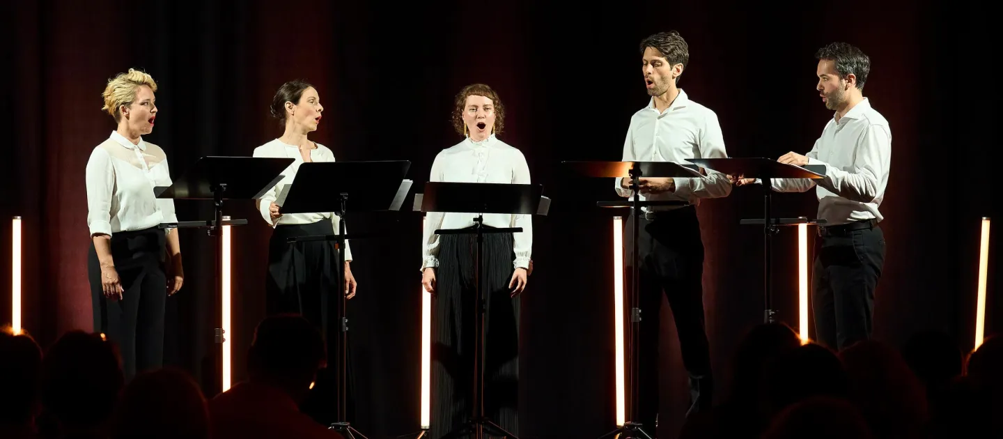 Szene aus "Konzert im KUB", 2024 im Kunsthaus Bregenz, fünf Sänger:innen mit weißem Hemd und schwarzer Hose, stehend hinter je einem Pult