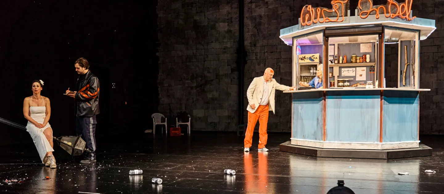 Szene aus "Lohn der Nacht", 2021 im Theater Kosmos, drei kostümierte Darstellende, Kiosk mit Darstellerin, vier Flaschen auf dem Boden