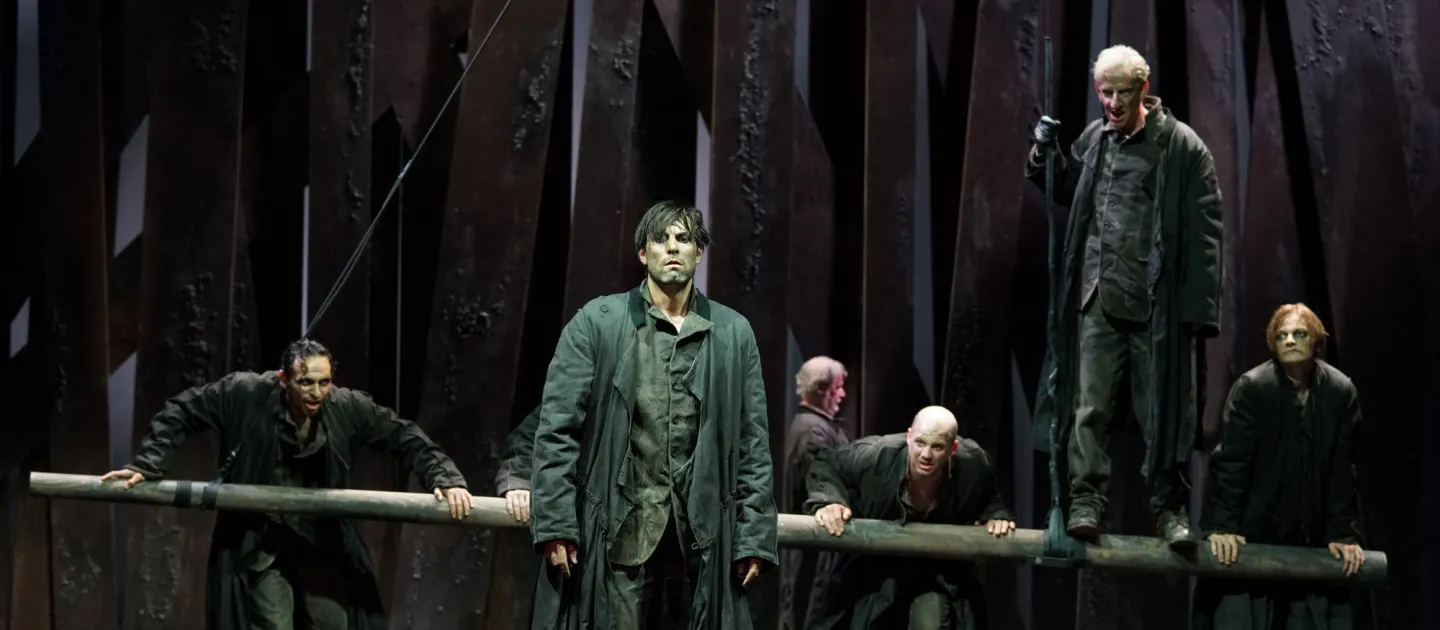 Szene aus "Michael Kohlhaas", 2021 im Theater am Kornmarkt, sechs dunkel kostümierte Darsteller, einer im Vordergrund, einer auf einer Holzabsperrung, die anderen hinter der Holzabsperrung