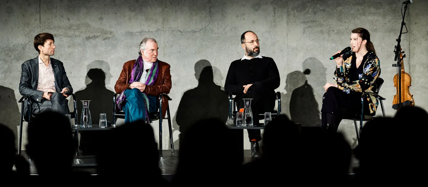 Szene aus "Einblick 1", 2022 im Kunsthaus Bregenz, vier Personen auf der Bühne, sitzend vor Publikum, rechts eine hängende Geige