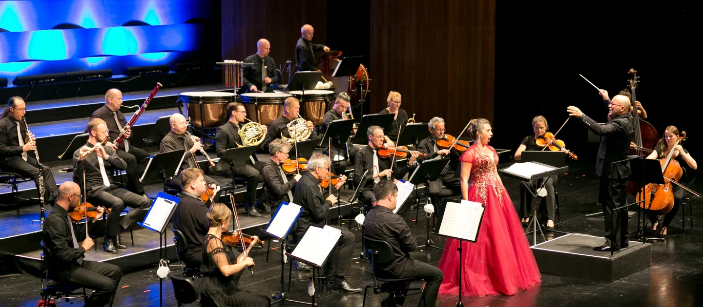 Szene aus "Viva Verdi - Viva L'Opera", 2020 im Festspielhaus, Musikerinnen auf der Bühne, Sängerin in rotem Kleid singt zentral
