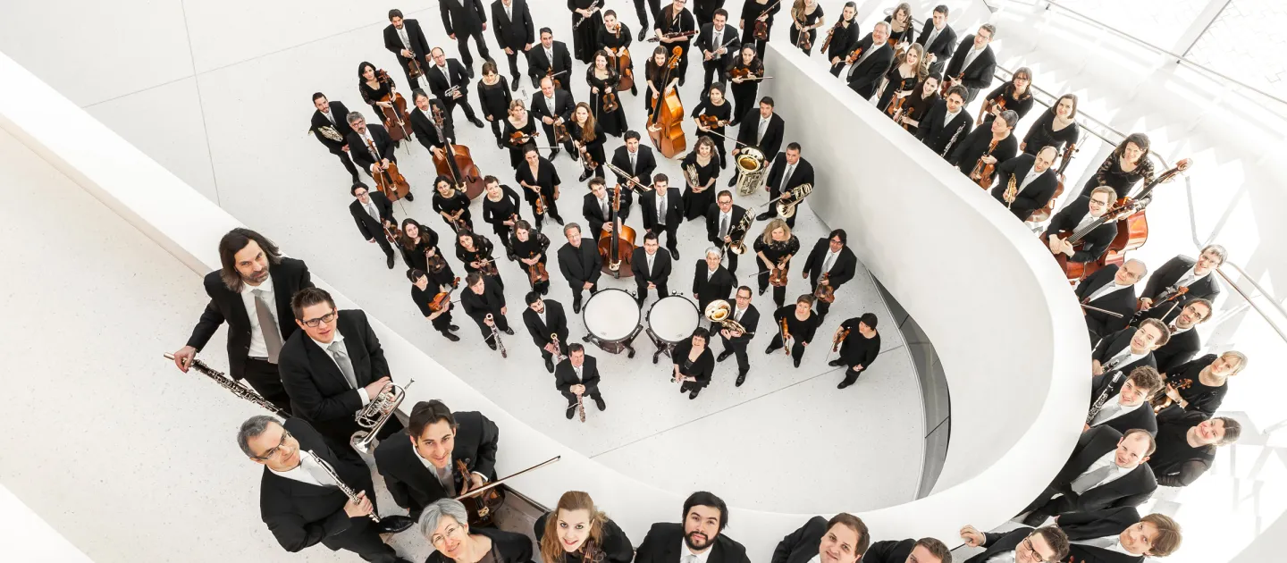 Symphonieorchester Vorarlberg, Musiker:innen in formeller Kleidung, Aufnahme aus Vogelperspektive in einem weißen Treppenhaus