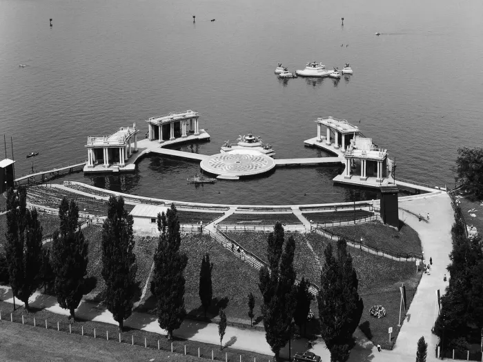 Szene aus "Der Bettelstudent", 1956 auf der Seebühne, im Mittelpunkt befindet sich eine runde Insel mit einem Boden in überwiegend schwarz-weißem Schachbrettmuster, am hinteren Bereich schließt sich ein schmaler Anbau mit vier Skulpturen und einem zentralen Brunnen an, links und rechts führt jeweils ein Steg zu zwei weiteren Inseln, auf denen je zwei tempelartige Gebäude mit Säulen stehen