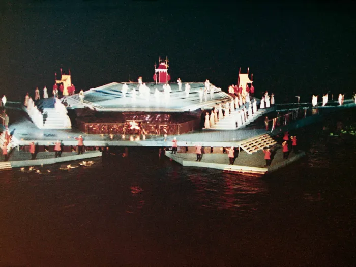 Szene aus "Die schöne Helena", 1966 auf der Seebühne, eine eckig gestaltete Plattform mit unterschiedlichen Höhenniveaus, die über Treppen miteinander verbunden sind, die Darstellenden sind auf verschiedenen Ebenen verteilt, teils in hellen, teils in roten Kostümen