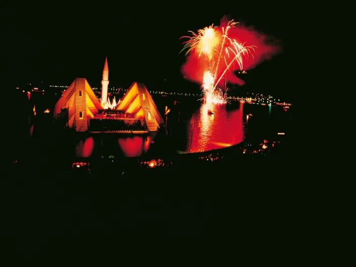 Szene aus "Die Entführung aus dem Serail", 1980 auf der Seebühne, rot beleuchtetes Bühnenbild mit emporragendem Turm, rechts davon ein Feuerwerk über dem Wasser