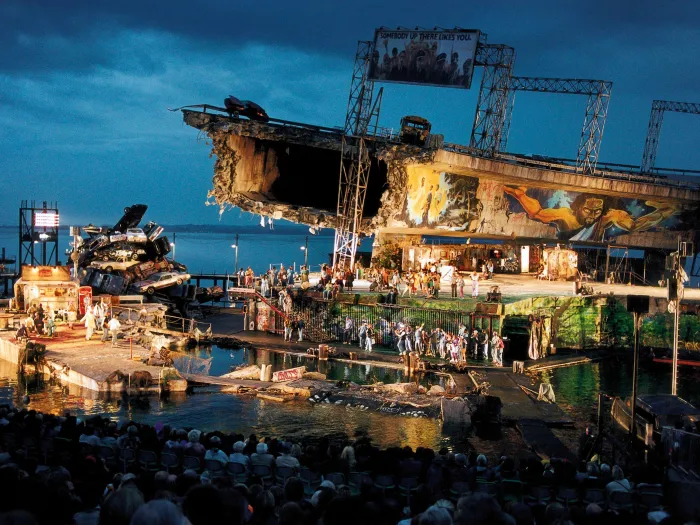 Szene aus "Porgy and Bess", 1997 auf der Seebühne, zerstörtes Brückenteil, bemalte Wände, ein Haufen aus Autos und viele kostümierte Darstellende 