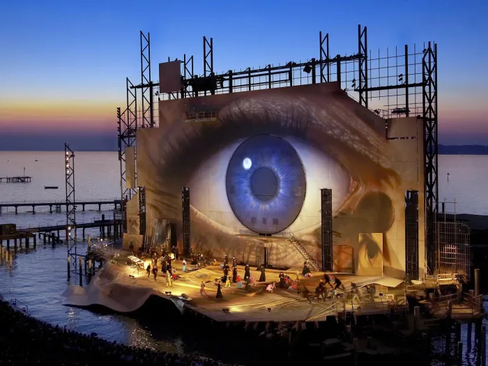 Szene aus "Tosca", 2007 auf der Seebühne, großes, flächendeckendes Auge auf der Rückwand, kostümierte Darstellende auf der Bühne
