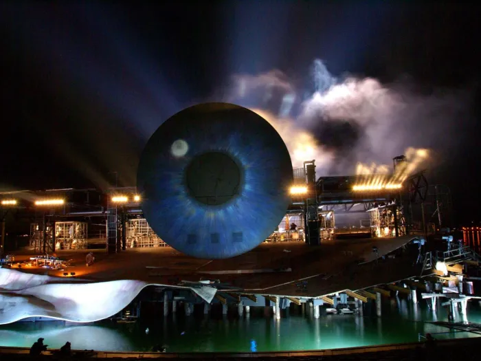 Szene aus "Tosca", 2008 auf der Seebühne, großes, blaufarbiges Auge, dahinter eine Gerüstkonstruktion und Nebel