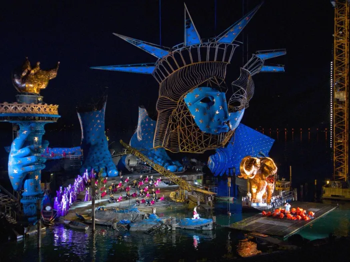 Szene aus "Aida", 2010 auf der Seebühne, Hintergrund mit großem blau-goldenen Freiheitstatue-Kopf und -Hand, viele kostümierte Darstellende und einem goldenen Elefanten