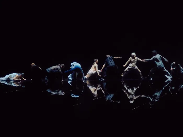 Tero Saarinen in einer modernen Tanzperformance, die sich in einer Linie mit dynamischen Posen auf einer reflektierenden schwarzen Bühne bewegen