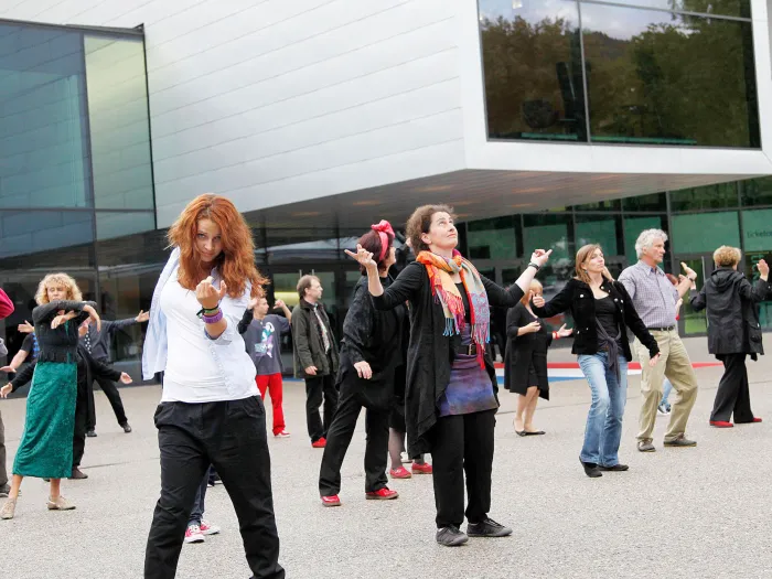 Szene aus "Der Beschwerdechor", 2011 auf dem Vorplatz des Festspielhauses, Gruppe von Menschen in Bewegung, im Hintergrund das Festspielhaus