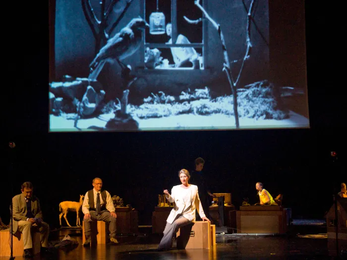 Szene aus "Der blonde Eckbert", 2011 im Theater am Kornmarkt, vier kostümierte Darstellende, drei im Vordergrund, einer im Hintergrund, im Hintergrund eine Leinwand mit einem schwarz-weißem Vogelbild