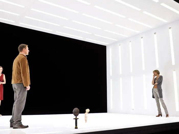 Szene aus "Peggy Pickit sieht das Gesicht Gottes", 2011 im Theater am Kornmarkt, vier kostümierte Darstellende in einem weißen Kubus ohne Vorder- und Rückwand, je zwei links und rechts, mittig zwei kleine Figuren