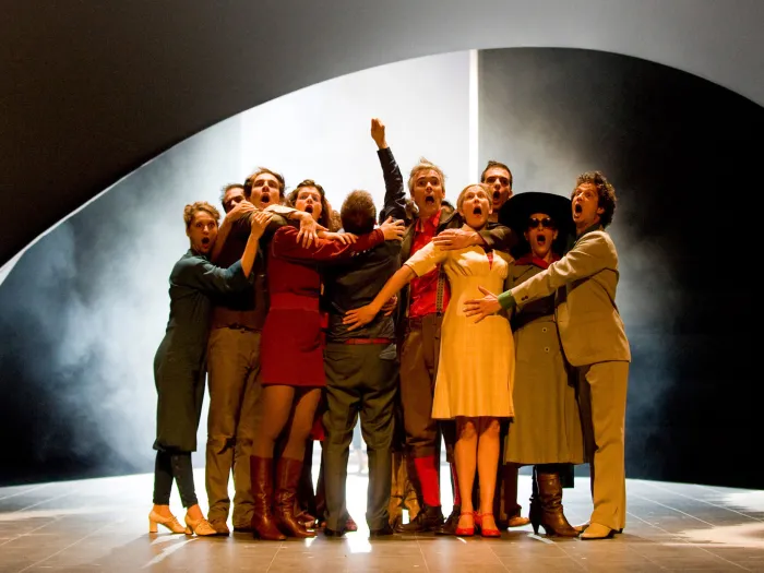 Szene aus "Das Allerheiligste trifft das Allermenschlichste - Petite messe solennelle", 2012 im Festspielhaus, zehn kostümierte Darstellende auf der Bühne gruppiert, im Hintergrund Nebel, dunkle Wände und Lichtstimmung