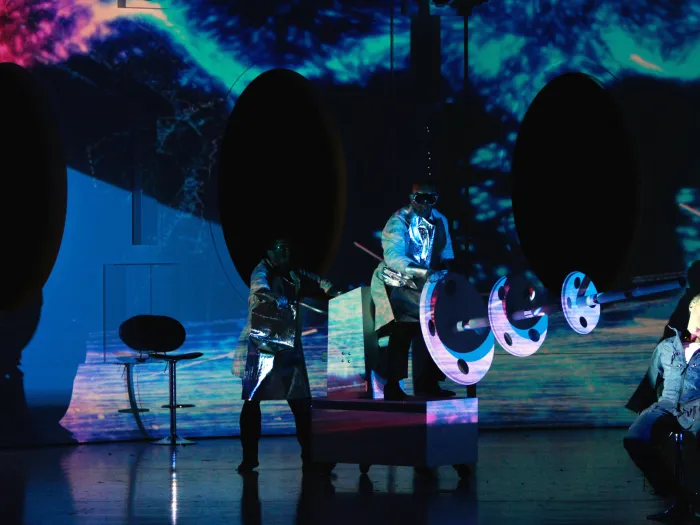 Szene aus "Solaris", 2012 im Festspielhaus, drei kostümierte Darstellende, bunte abstrakte Projektionen im Hintergrund