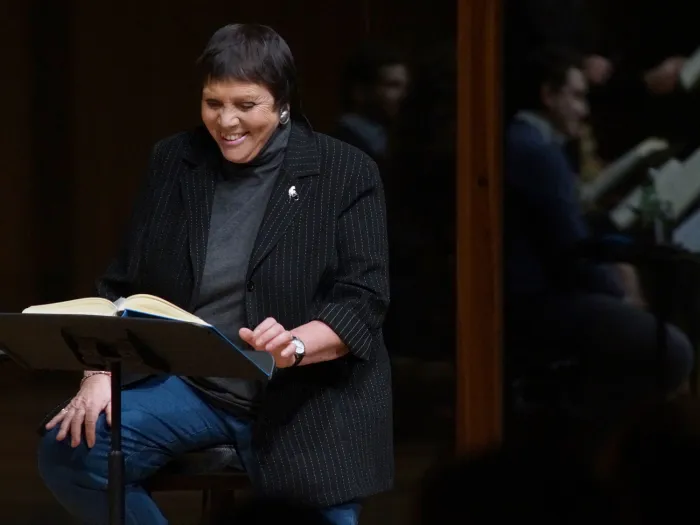 Szene aus "Meisterklasse B. Fassbaender", 2017 im Festspielhaus, B. Fassbaender sitzt lächelnd auf einem Stuhl, vor ihr ein Pult
