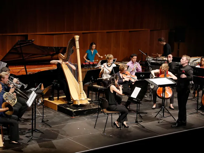 Szene aus "Opus XXI", 2017 im Festspielhaus, Musiker:innen auf der Bühne, Dirigent steht davor