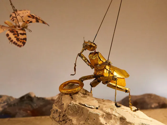 Szene aus "Ring in 90 Minuten", 2017 im Festspielhaus, goldfarbener Käfer als Marionette hält einen goldenen Ring, vor ihm schwebt ein Schmetterling mit braunen Flecken