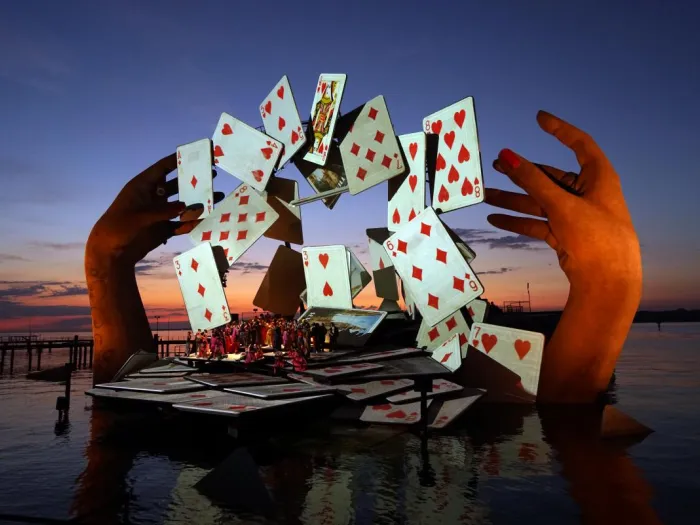 Szene aus "Carmen", 2017 auf der Seebühne, große Hände über dem Wasser, die Spielkarten in einem Bogen schweben lassen