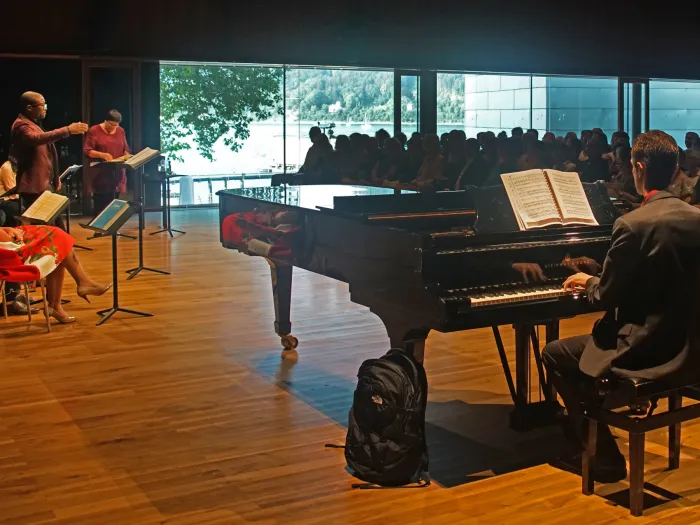 Szene aus "Meisterklasse Brigitte Fassbaender", 2018 im Festspielhaus, Flügel mit Pianist, vier Sänger:innen, davon eine Person stehend, Brigitte Fassbaender am Pult stehend, Publikum schaut zu und hört zu