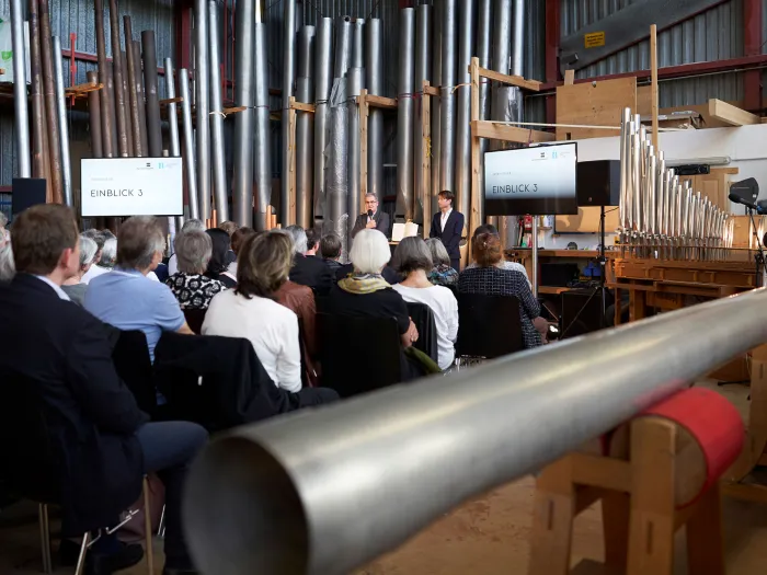 Szene aus "Einblick 3: Das Instrument", 2019 bei Rieger-Orgelbau Schwarzach, Publikum hört zwei Personen zu, umgeben Orgelpfeifen