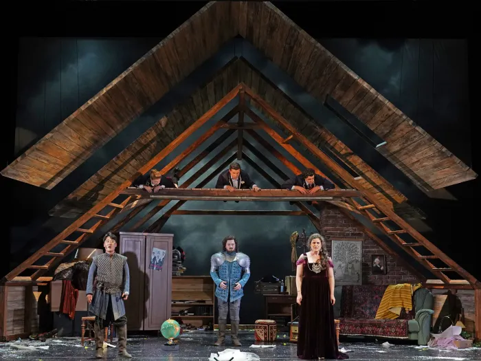 Szene aus "Armida", 2022 im Theater am Kornmarkt, sechs kostümierte Darstellende, darunter Ritterrüstungen und mittelalterliche Kleidung, drei im Dachstuhl liegend, drei in der Stube stehend, im Hintergrund Möbel
