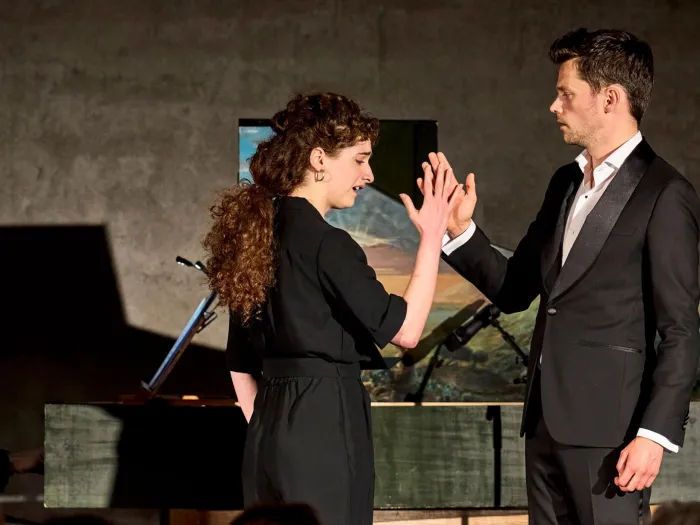 Szene aus "Konzert im KUB", 2023 im Kunsthaus Bregenz, drei Personen, zwei im Vordergrund an der rechten Hand haltend, eine im Hintergrund am Flügel